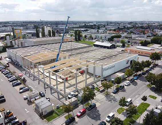 Luftaufnahme einer Industriehalle im Bau, moderne Infrastruktur, Kräne und Baumaschinen im Einsatz.