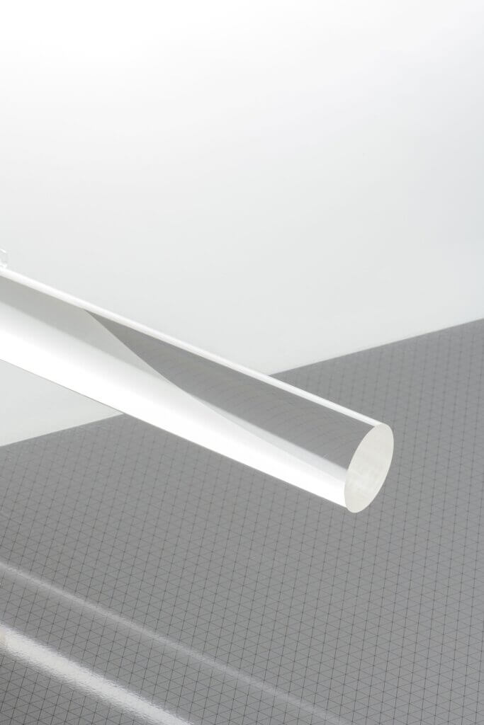 Transparenter Kunststoffzylinder auf grauem, kariertem Hintergrund für moderne industrielle Designs.
