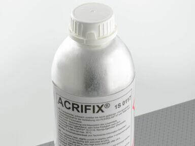 Flasche mit Acrifix Kleber auf grauer Fläche, geeignet zum Reparieren und Verkleben von Kunststoffmaterialien.